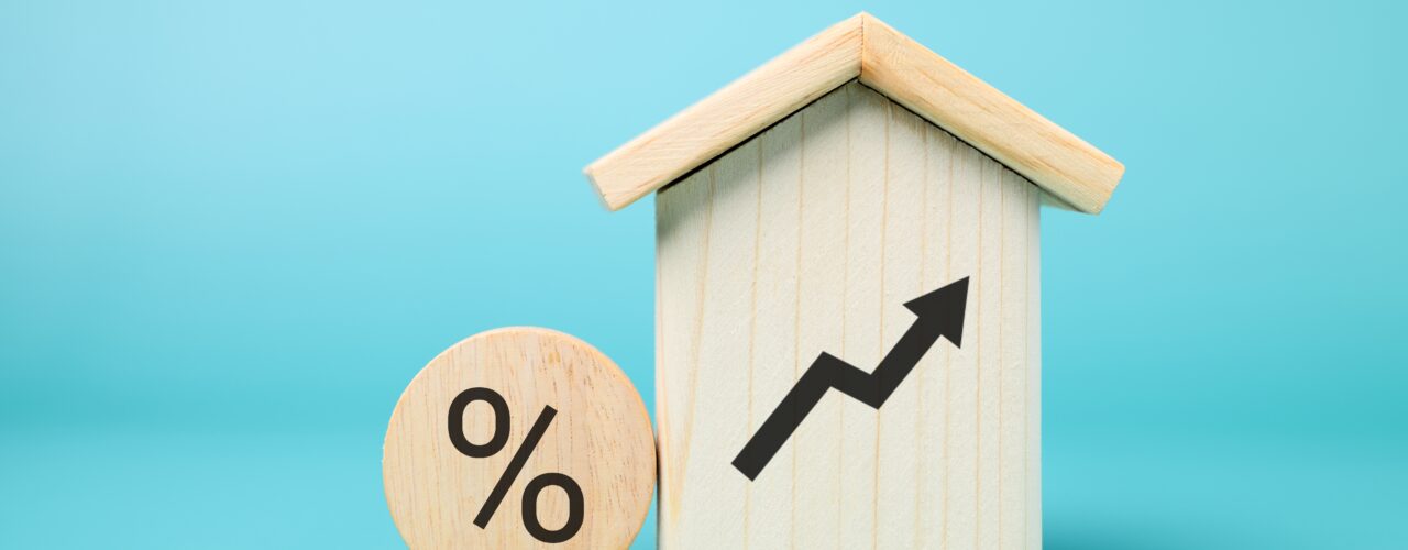 A wooden house with a rising arrow on it and a round block with a percentage sign of to signify rent increase.