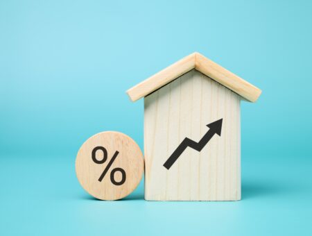 A wooden house with a rising arrow on it and a round block with a percentage sign of to signify rent increase.